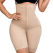 En kvinde iført beige figurformende shorts med skulderstropper, høj talje og knaplukning, der går fra skuldrene til lårene.