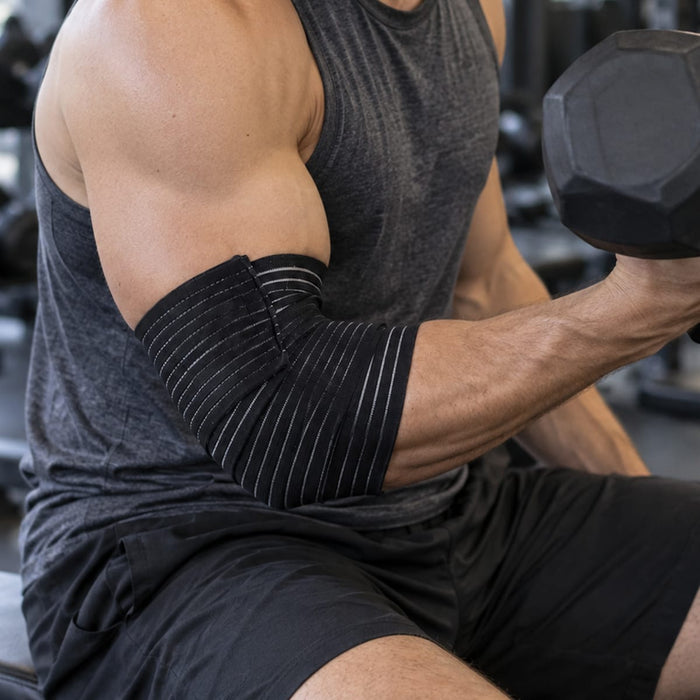 En mand træner med håndvægte i fitnesscentret iført et elastisk armbånd, der giver ekstra støtte og kompression ved albuen.